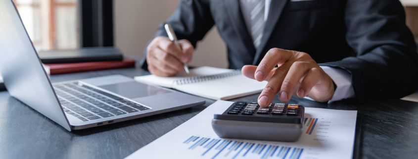 Front view of a man working on financial documents with calculator and laptop