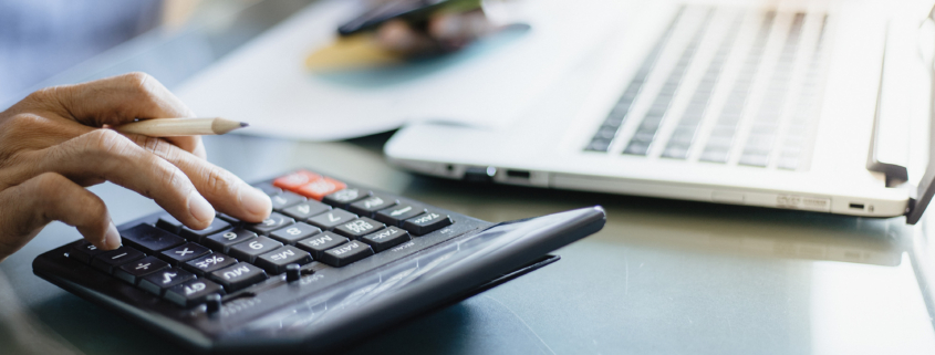 Side view of someone using a calculator while their laptop is sitting open in front of them, close up view